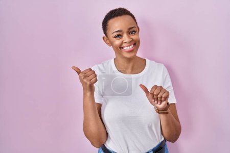 Photo for Beautiful african american woman standing over pink background pointing to the back behind with hand and thumbs up, smiling confident - Royalty Free Image