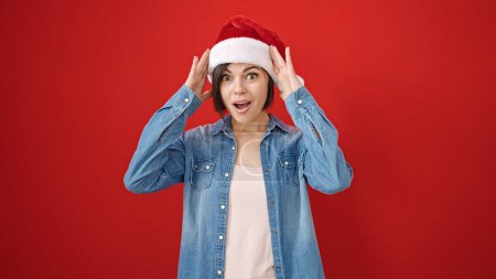 Téléchargez les photos : Jeune femme caucasienne expression surprise portant chapeau de Noël sur fond rouge isolé - en image libre de droit
