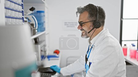 Téléchargez les photos : Jeune scientifique hispanique attrayant, un homme aux cheveux gris, absorbé dans une conférence en ligne via ordinateur dans le laboratoire animé, plongé dans la recherche médicale de pointe. - en image libre de droit