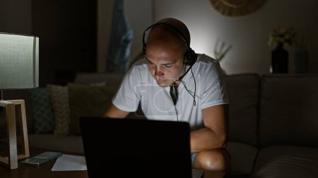 Téléchargez les photos : Jeune homme hispanique utilisant ordinateur portable et écouteurs assis sur le canapé à la maison - en image libre de droit