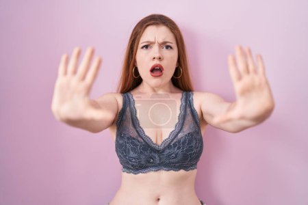 Photo for Redhead woman wearing lingerie over pink background doing stop gesture with hands palms, angry and frustration expression - Royalty Free Image