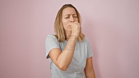 Photo for Caught a chill? beautiful young blonde woman coughing, showing flu-like symptoms over an isolated pink background. a cool yet serious expression, the rising concern of covid-19 evident. - Royalty Free Image