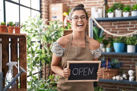 Photo for Hispanic woman working at florist holding open sign smiling and laughing hard out loud because funny crazy joke. - Royalty Free Image