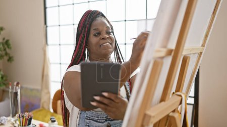 Photo for Confident, beautiful african american woman artist happily drawing on touchpad, bringing creativity to life in modern art studio setting. - Royalty Free Image