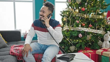 Téléchargez les photos : Jeune homme latino parlant au téléphone célébrant Noël à la maison - en image libre de droit