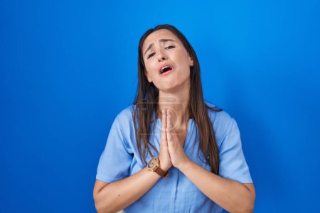 Photo for Young brunette woman standing over blue background begging and praying with hands together with hope expression on face very emotional and worried. begging. - Royalty Free Image