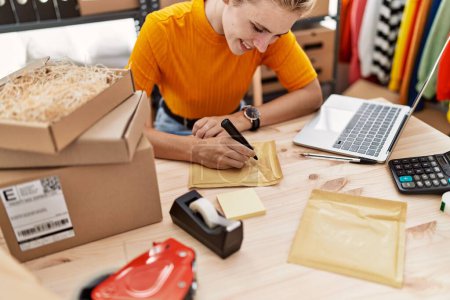Téléchargez les photos : Jeune femme blonde ecommerce travailleur d'affaires en utilisant l'écriture d'ordinateur portable sur le paquet au bureau - en image libre de droit