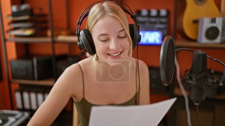 Téléchargez les photos : Jeune femme blonde musicienne lisant une partition musicale chantant au studio de musique - en image libre de droit