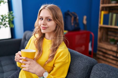 Photo for Young blonde woman drinking coffee sitting on sofa at street - Royalty Free Image