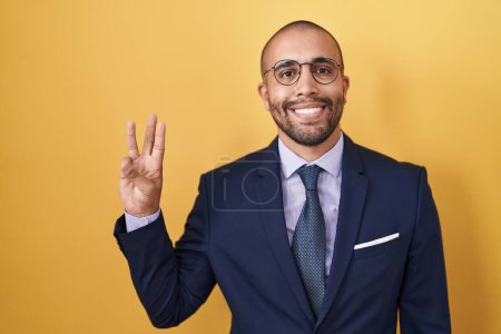 Photo for Hispanic man with beard wearing suit and tie showing and pointing up with fingers number three while smiling confident and happy. - Royalty Free Image