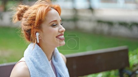 Téléchargez les photos : Jeune rousse femme portant des vêtements de sport écoutant de la musique souriant au parc - en image libre de droit
