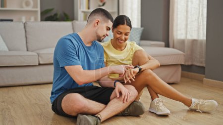 Photo for Beautiful couple kicking off their fitness journey together, sitting on the living room floor, confidently starting the stopwatch for an at-home yoga workout. - Royalty Free Image
