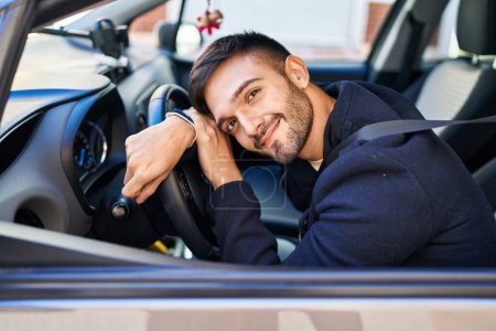 Téléchargez les photos : Jeune homme hispanique souriant confiant appuyé sur le volant dans la rue - en image libre de droit