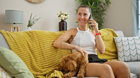 Photo for Young caucasian woman with dog playing sitting on the sofa speaking on the phone at home - Royalty Free Image