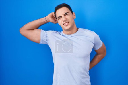 Photo for Young hispanic man standing over blue background stretching back, tired and relaxed, sleepy and yawning for early morning - Royalty Free Image