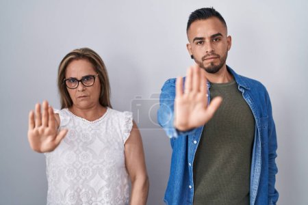 Photo for Hispanic mother and son standing together doing stop sing with palm of the hand. warning expression with negative and serious gesture on the face. - Royalty Free Image