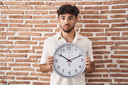 Photo for Arab man with beard holding big clock relaxed with serious expression on face. simple and natural looking at the camera. - Royalty Free Image