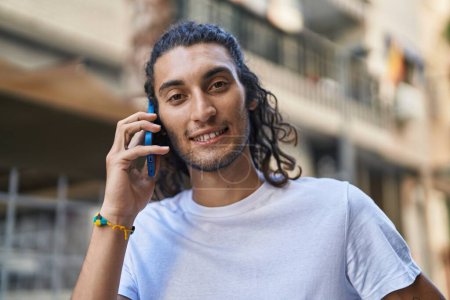 Téléchargez les photos : Jeune homme hispanique souriant confiant parler sur le smartphone à la rue - en image libre de droit