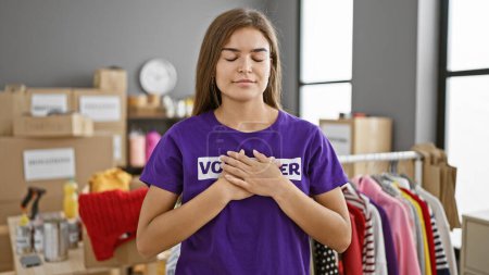 Photo for Emotional portrait of a beautiful, young hispanic woman working indoors at a charity center, hands on chest, closing her eyes in concentrated devotion to community service. - Royalty Free Image