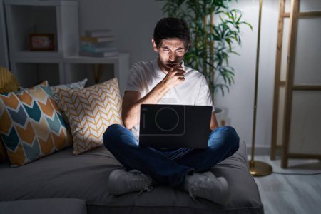 Téléchargez les photos : Jeune homme hispanique utilisant un ordinateur portable à la maison la nuit se sentant mal et toussant comme symptôme du rhume ou de la bronchite. concept de soins de santé. - en image libre de droit