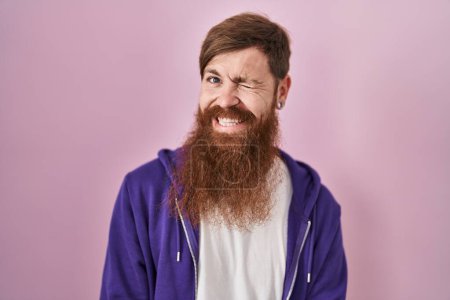Téléchargez les photos : Homme caucasien avec longue barbe debout sur fond rose clin d'oeil en regardant la caméra avec expression sexy, gai et heureux visage. - en image libre de droit