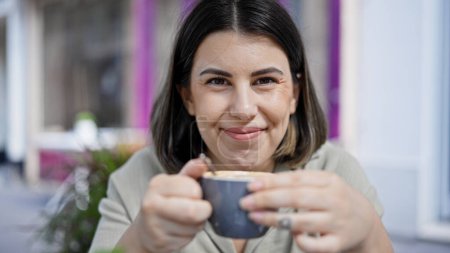 Téléchargez les photos : Jeune belle femme hispanique buvant du café assis sur la table à la cafétéria extérieure - en image libre de droit