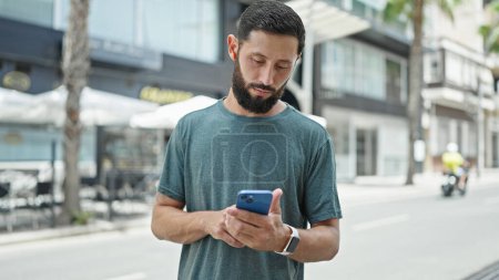 Téléchargez les photos : Jeune homme hispanique utilisant smartphone et écouteurs dans la rue - en image libre de droit