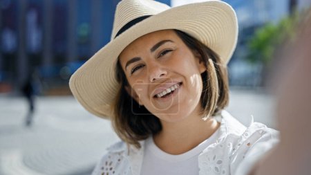 Foto de Hermosa joven hispana tomando foto selfie sonriendo confiada usando sombrero de verano en el edificio del Premio Nobel - Imagen libre de derechos