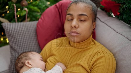 Foto de Madre e hijo celebrando la Navidad durmiendo en el sofá mientras amamantan al bebé en casa - Imagen libre de derechos