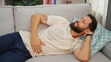 Photo for Young hispanic man suffering for stomach ache lying on sofa at home - Royalty Free Image