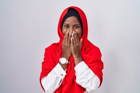 Téléchargez les photos : Jeune femme arabe portant l'écharpe traditionnelle islamique hijab rire et rire embarrassé couvrant la bouche avec les mains, les commérages et le concept de scandale - en image libre de droit