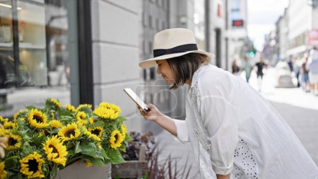 Téléchargez les photos : Belle jeune femme hispanique souriante prenant des photos de fleurs dans les rues de Stockholm - en image libre de droit