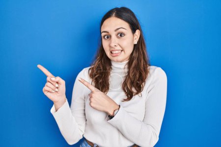 Photo for Young hispanic woman standing over blue background pointing aside worried and nervous with both hands, concerned and surprised expression - Royalty Free Image