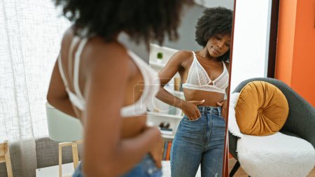 Téléchargez les photos : Femme afro-américaine portant un jean regardant le miroir à la maison - en image libre de droit