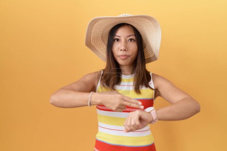 Photo for Middle age chinese woman wearing summer hat over yellow background in hurry pointing to watch time, impatience, upset and angry for deadline delay - Royalty Free Image