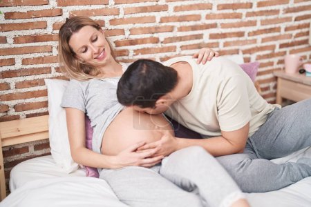 Téléchargez les photos : Homme et femme couple baisers ventre assis sur le lit à la chambre - en image libre de droit