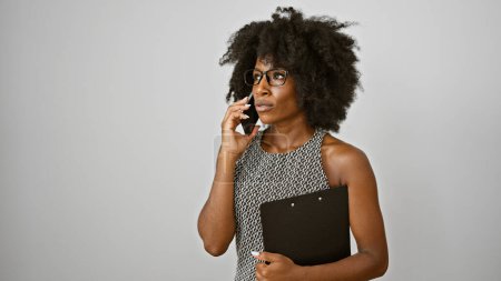 Téléchargez les photos : Femme afro-américaine ouvrière parlant sur smartphone tenant presse-papiers sur fond blanc isolé - en image libre de droit