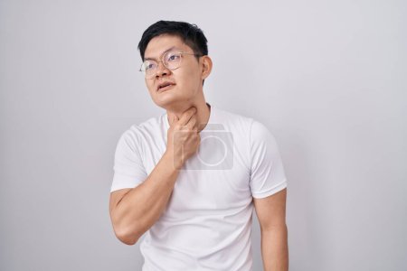 Foto de Joven asiático de pie sobre fondo blanco tocando doloroso cuello, dolor de garganta para gripe, clod e infección - Imagen libre de derechos