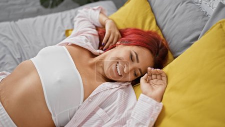 Photo for Beautiful young redhead woman wakes up stretching her arms in bed, smiling in the comfort of her cozy bedroom, exuding happiness and confidence. - Royalty Free Image