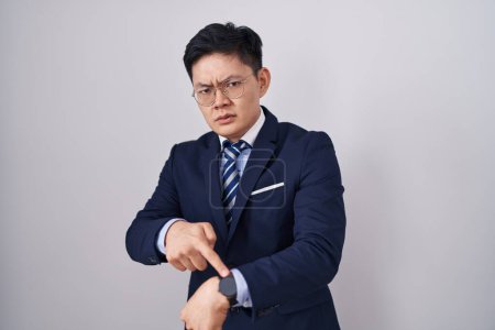 Téléchargez les photos : Jeune homme asiatique portant costume d'affaires et cravate à la hâte pointant pour regarder le temps, l'impatience, bouleversé et en colère pour délai - en image libre de droit