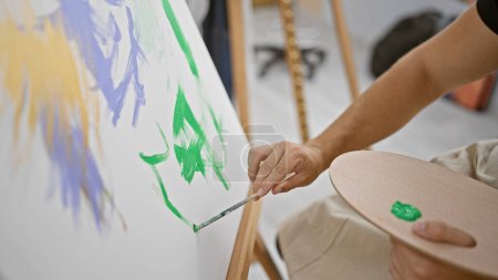 Photo for Handsome young hispanic man, an aspiring artist, passionately drawing in the heart of his art studio, carefully holding his paintbrush hand - Royalty Free Image