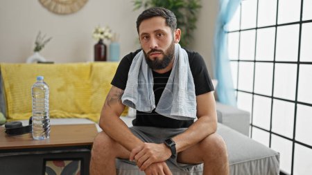 Photo for Young hispanic man sitting on sofa with serious face at home - Royalty Free Image