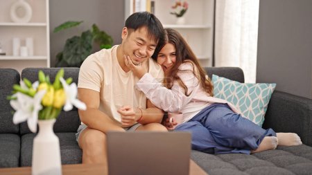 Téléchargez les photos : Homme et femme couple assis sur le canapé ayant appel vidéo boire du café à la maison - en image libre de droit