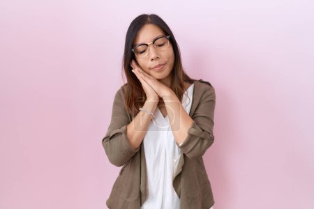 Téléchargez les photos : Moyen Age femme chinoise portant des lunettes sur fond rose dormir fatigué rêver et posant avec les mains ensemble tout en souriant avec les yeux fermés. - en image libre de droit