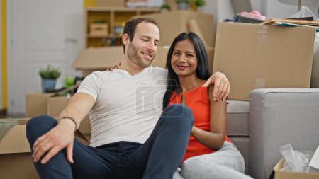 Foto de Hermosa pareja abrazándose el uno al otro sentado en el suelo sonriendo en casa nueva - Imagen libre de derechos