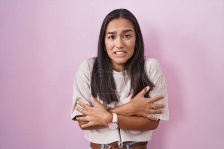 Foto de Young hispanic woman standing over pink background shaking and freezing for winter cold with sad and shock expression on face - Imagen libre de derechos
