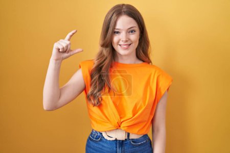 Photo for Caucasian woman standing over yellow background smiling and confident gesturing with hand doing small size sign with fingers looking and the camera. measure concept. - Royalty Free Image