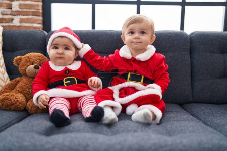 Photo for Adorable boy and girl wearing christmas clothes sitting on sofa at home - Royalty Free Image
