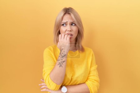 Photo for Young caucasian woman wearing yellow sweater looking stressed and nervous with hands on mouth biting nails. anxiety problem. - Royalty Free Image