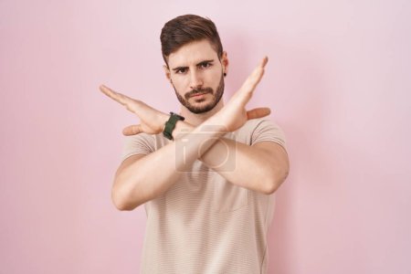 Téléchargez les photos : Homme hispanique avec barbe debout sur fond rose expression de rejet croisant les bras faisant signe négatif, visage en colère - en image libre de droit